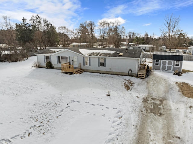 snow covered house featuring a shed and a wooden deck