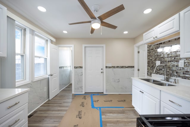 kitchen with wood-type flooring, sink, tile walls, and white cabinets