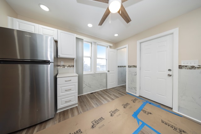 kitchen featuring dark wood-type flooring, stainless steel refrigerator, ceiling fan, white cabinetry, and tile walls