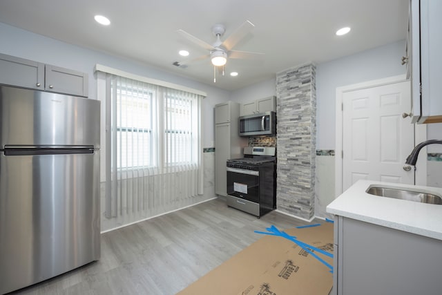 kitchen with sink, gray cabinetry, appliances with stainless steel finishes, ceiling fan, and light hardwood / wood-style floors