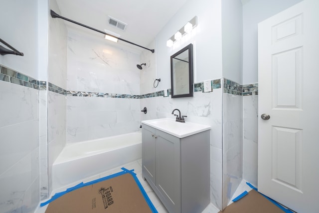 bathroom with vanity, tiled shower / bath combo, and tile walls