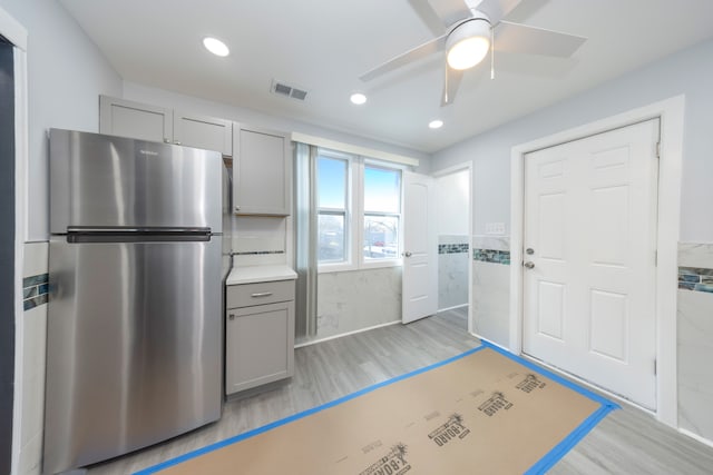 kitchen featuring stainless steel refrigerator, gray cabinetry, tile walls, ceiling fan, and light wood-type flooring