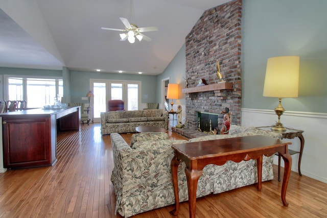 living room featuring a brick fireplace, light hardwood / wood-style floors, high vaulted ceiling, and ceiling fan