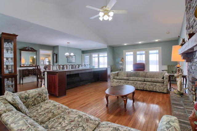 living room featuring ceiling fan with notable chandelier, high vaulted ceiling, light hardwood / wood-style floors, and a brick fireplace