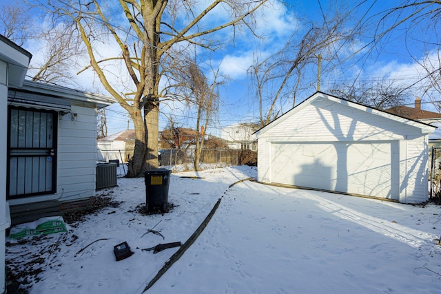 snowy yard with a garage, an outdoor structure, and central AC unit