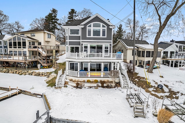 snow covered back of property with stairway, a residential view, a wooden deck, and a sunroom