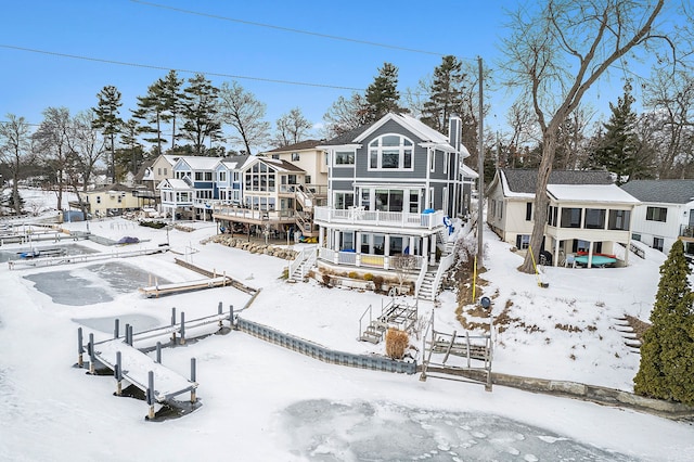 snow covered rear of property featuring a garage, a sunroom, a residential view, stairway, and fence