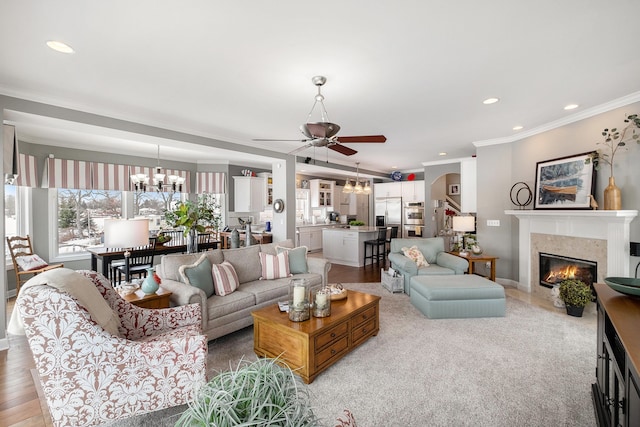 living area with recessed lighting, ceiling fan with notable chandelier, a fireplace, ornamental molding, and light wood-type flooring