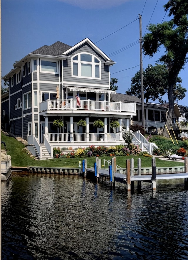 back of property with a water view, a lawn, and roof with shingles