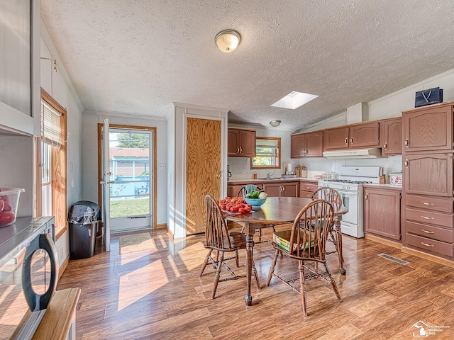 dining space with lofted ceiling with skylight, sink, a textured ceiling, and light hardwood / wood-style floors