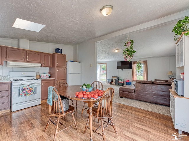 kitchen featuring lofted ceiling with skylight, light wood-type flooring, a textured ceiling, and white appliances