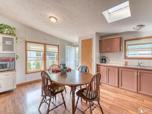 dining area with sink, lofted ceiling with skylight, light hardwood / wood-style floors, and a textured ceiling