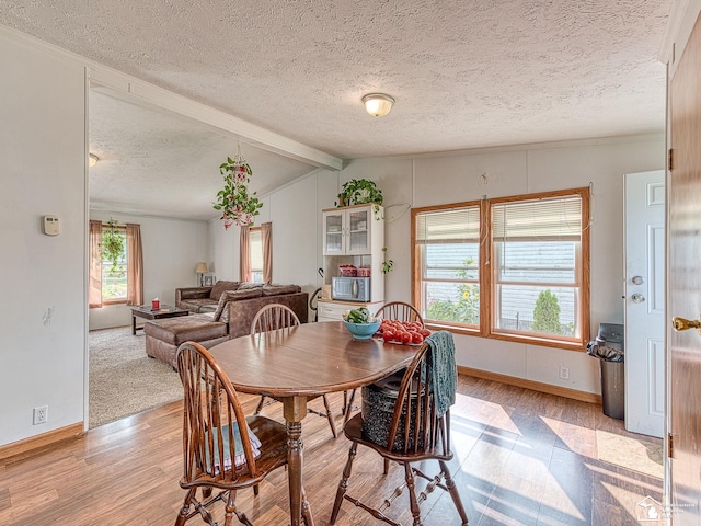 dining space with a healthy amount of sunlight, lofted ceiling with beams, light hardwood / wood-style flooring, and a textured ceiling