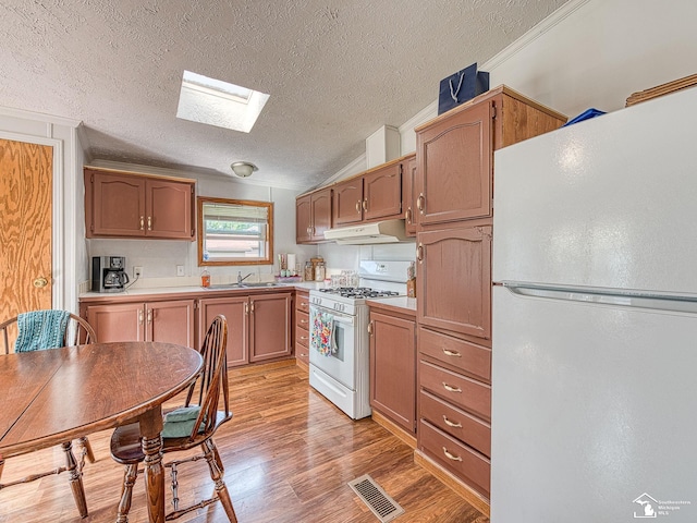 kitchen with sink, white appliances, vaulted ceiling with skylight, a textured ceiling, and light wood-type flooring