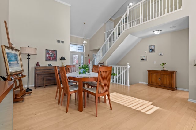 dining area with ornamental molding, a towering ceiling, an inviting chandelier, and light hardwood / wood-style floors