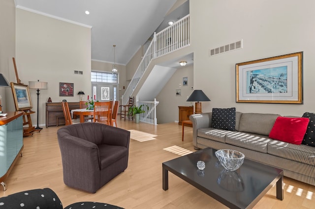 living room featuring light hardwood / wood-style flooring, ornamental molding, a chandelier, and a high ceiling