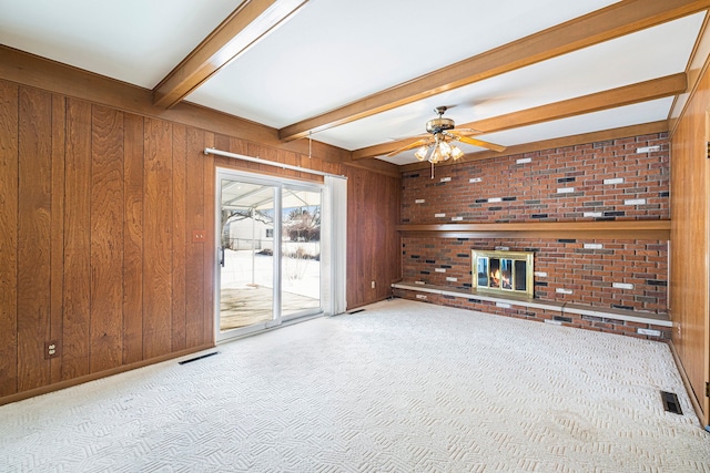 unfurnished living room with a brick fireplace, light colored carpet, beam ceiling, and wood walls