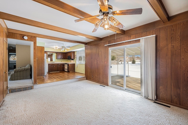 unfurnished living room featuring sink, light colored carpet, wooden walls, ceiling fan, and beam ceiling