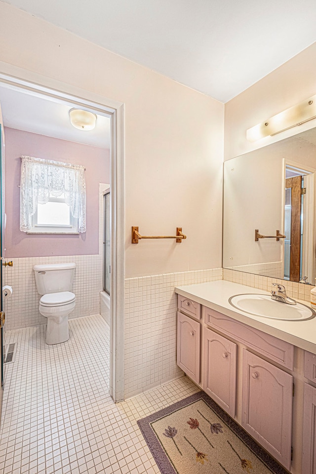 bathroom with tile walls, tile patterned flooring, vanity, toilet, and a shower with door