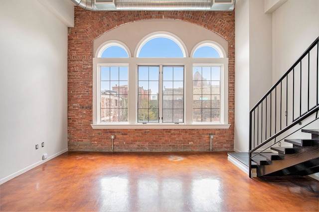 interior space featuring a high ceiling, brick wall, and concrete floors