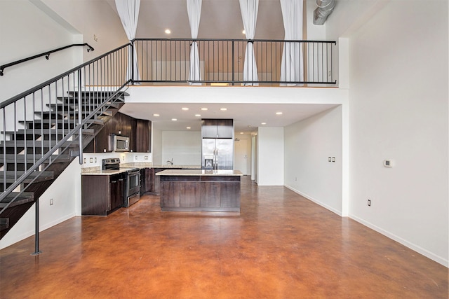 kitchen with stainless steel appliances, a kitchen island, a high ceiling, and dark brown cabinetry