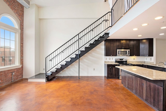 kitchen with a towering ceiling, stainless steel appliances, dark brown cabinetry, light stone countertops, and concrete floors