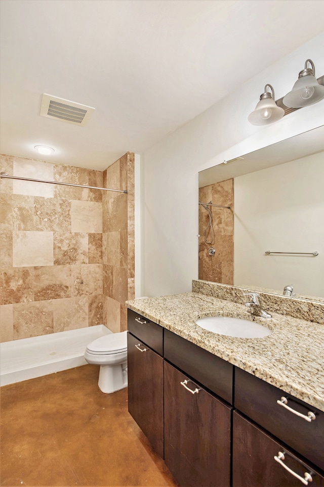 bathroom with concrete flooring, vanity, tiled shower, and toilet