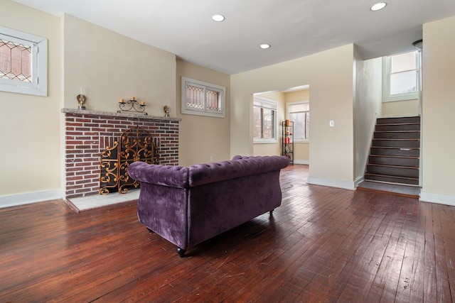 living room with a brick fireplace and dark wood-type flooring