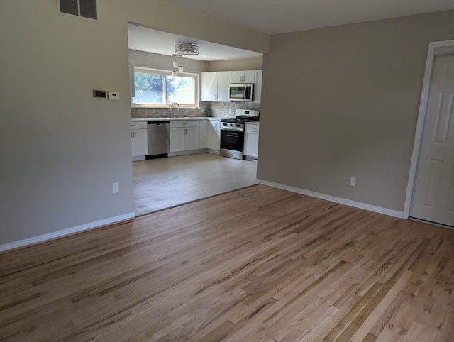 kitchen with hanging light fixtures, light wood-type flooring, appliances with stainless steel finishes, decorative backsplash, and white cabinets