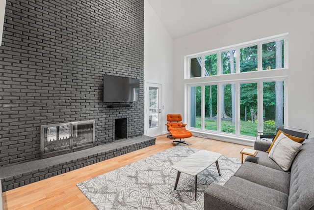 living room with a brick fireplace, wood-type flooring, and high vaulted ceiling