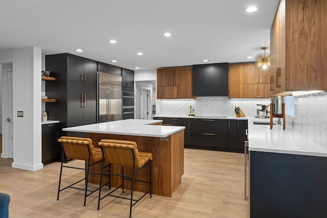 kitchen with built in fridge, a kitchen island, range hood, a breakfast bar area, and light hardwood / wood-style flooring