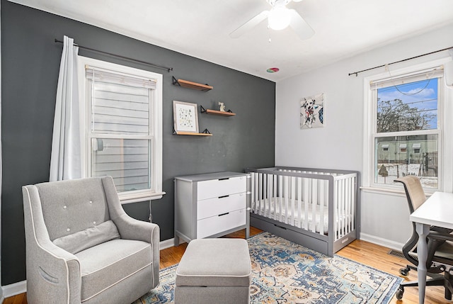 bedroom featuring a nursery area, ceiling fan, and light wood-type flooring