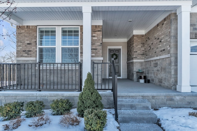 snow covered property entrance with brick siding and a porch