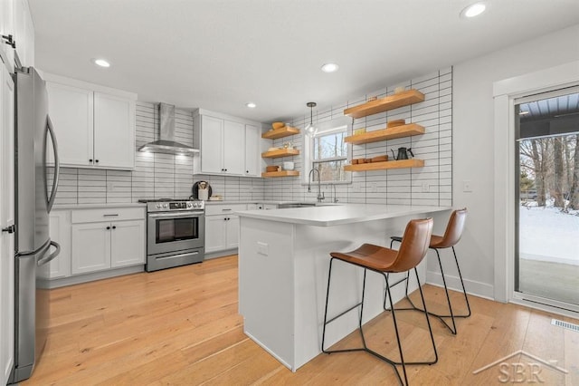 kitchen with appliances with stainless steel finishes, a breakfast bar, white cabinets, kitchen peninsula, and wall chimney range hood