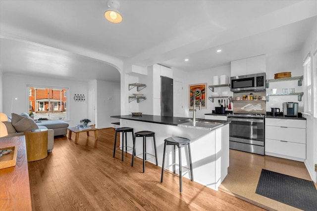 kitchen with appliances with stainless steel finishes, light hardwood / wood-style floors, a breakfast bar area, and white cabinets