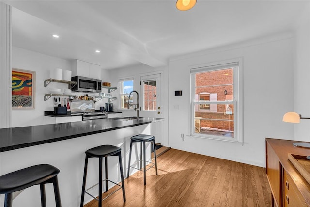 kitchen featuring sink, light hardwood / wood-style flooring, appliances with stainless steel finishes, white cabinetry, and a kitchen breakfast bar