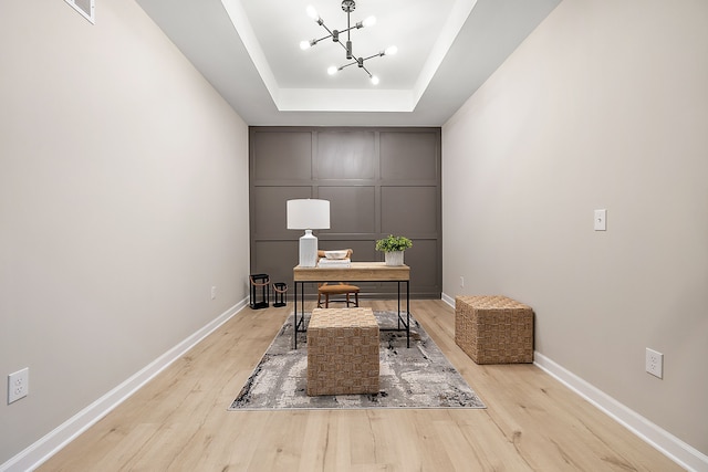 office area with an inviting chandelier, a raised ceiling, and light wood-type flooring