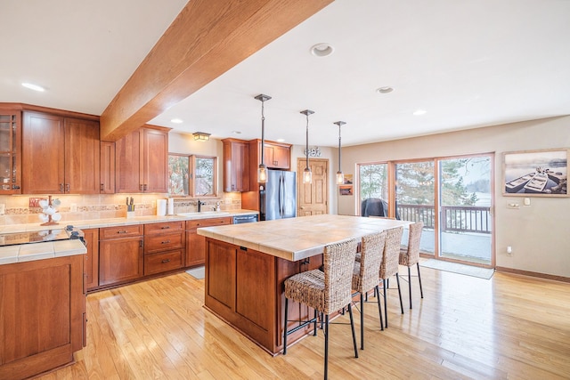 kitchen with a kitchen island, appliances with stainless steel finishes, sink, hanging light fixtures, and light hardwood / wood-style floors