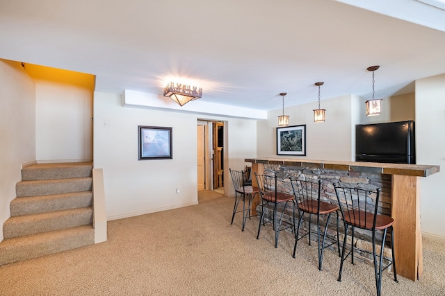 kitchen with a kitchen bar, light colored carpet, hanging light fixtures, and black fridge