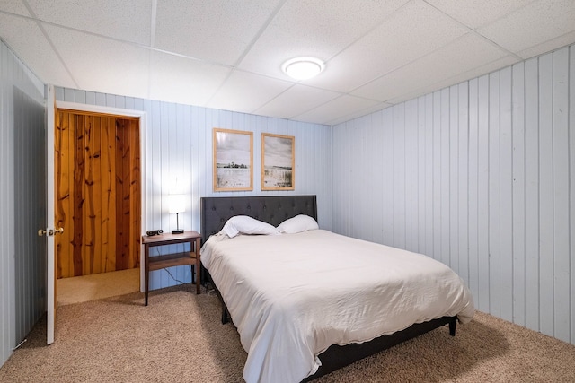 carpeted bedroom with a paneled ceiling and wood walls