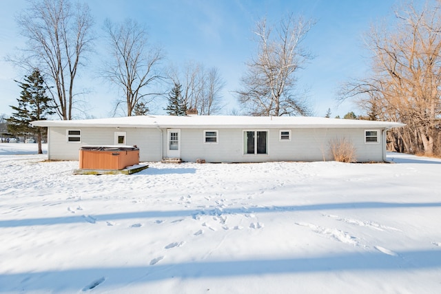 snow covered rear of property with a hot tub