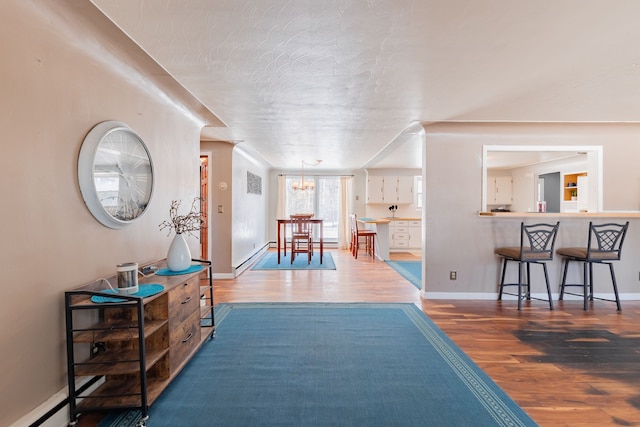 hall with hardwood / wood-style flooring, a baseboard heating unit, a textured ceiling, and a notable chandelier