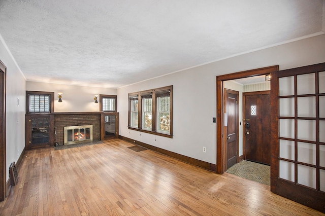 unfurnished living room featuring ornamental molding, a textured ceiling, a brick fireplace, and light hardwood / wood-style flooring