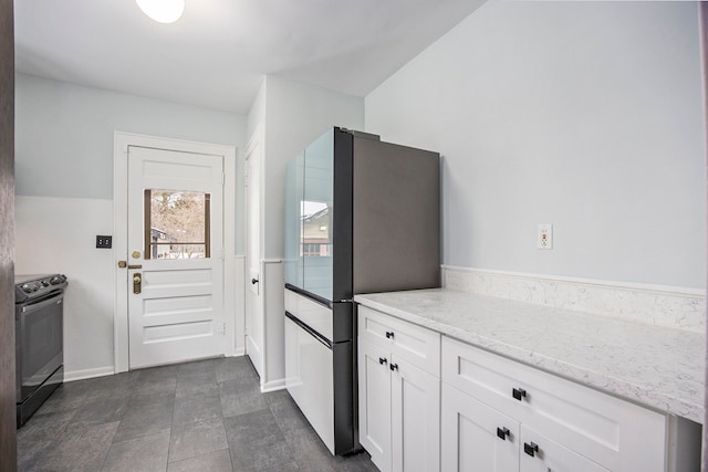 kitchen featuring white cabinetry, stainless steel refrigerator, light stone counters, and black range with electric cooktop