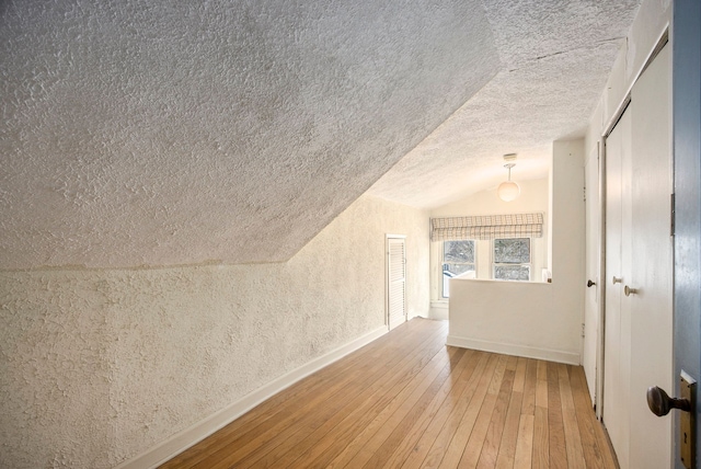 additional living space with wood-type flooring, vaulted ceiling, and a textured ceiling