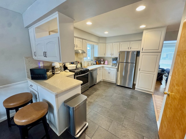 kitchen featuring a breakfast bar area, white cabinetry, appliances with stainless steel finishes, kitchen peninsula, and backsplash