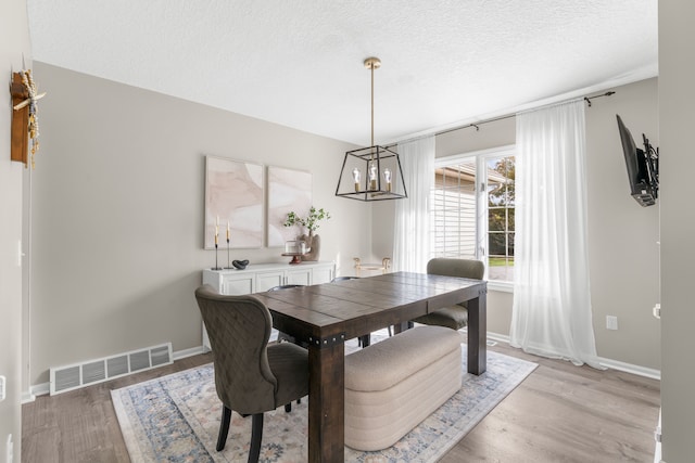 dining space featuring an inviting chandelier, light hardwood / wood-style floors, and a textured ceiling