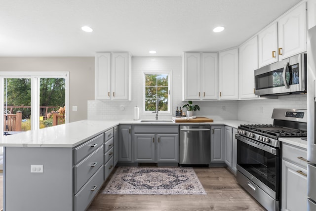 kitchen with appliances with stainless steel finishes, hardwood / wood-style floors, sink, gray cabinetry, and kitchen peninsula