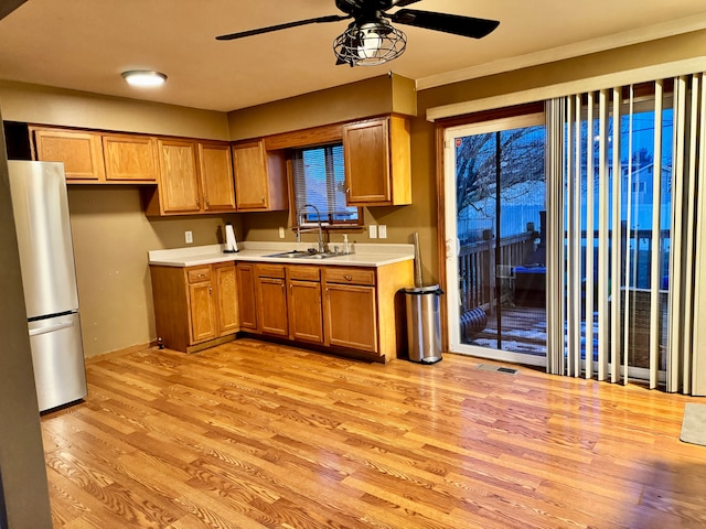 kitchen with stainless steel refrigerator, ceiling fan, sink, and light hardwood / wood-style flooring