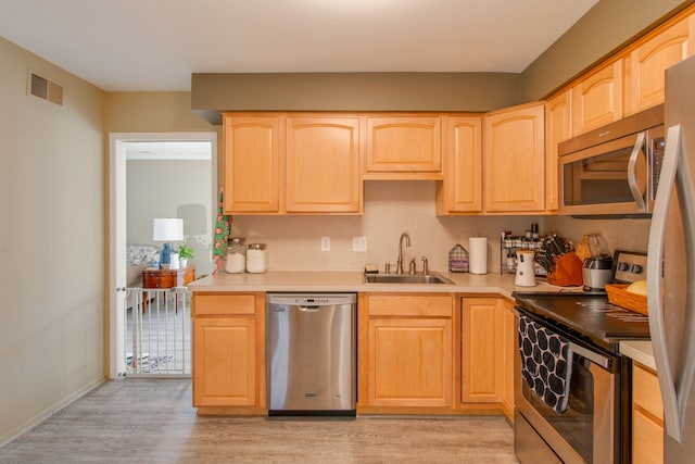 kitchen featuring stainless steel appliances, sink, light brown cabinets, and light wood-type flooring